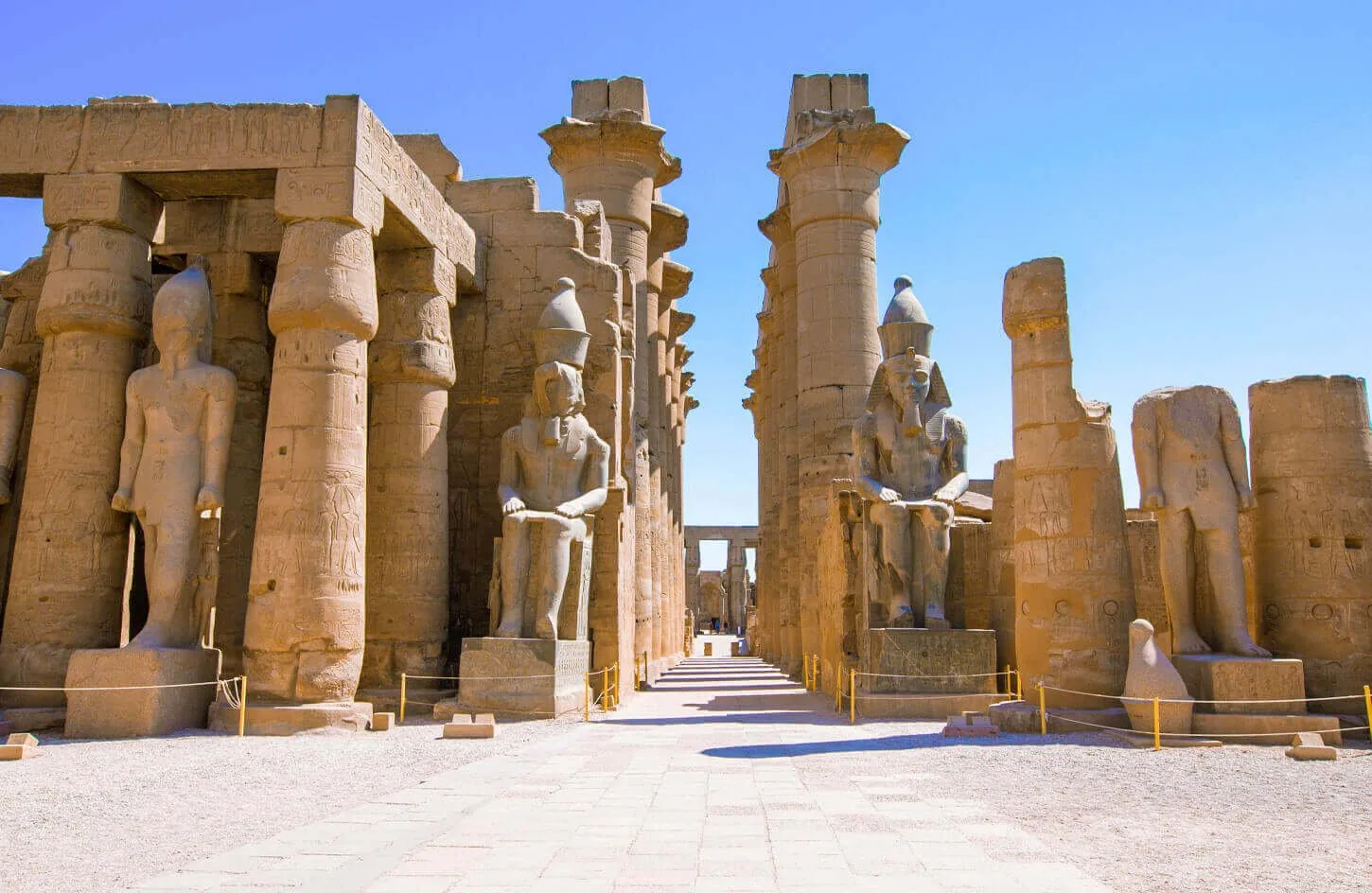 seated granite royal statues of ramesses ii flanking the entrance pylon of luxor temple under blue sky