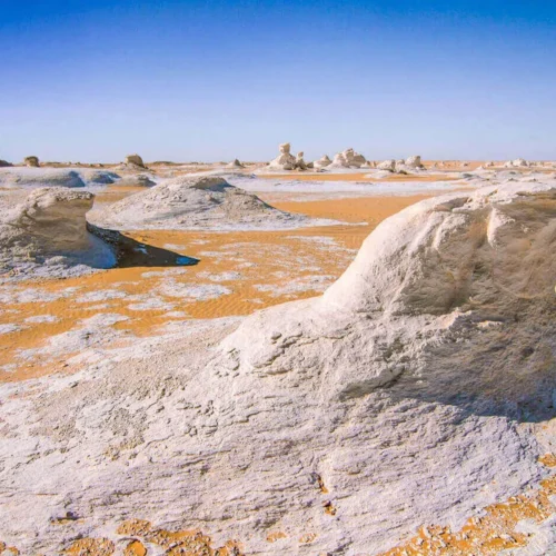 travelers exploring surreal white chalk limestone formations under bright blue skies in the egyptian white desert