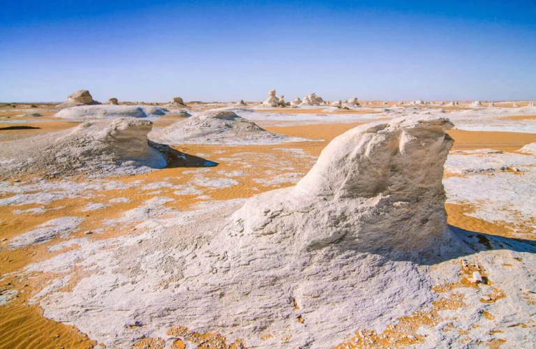 travelers exploring surreal white chalk limestone formations under bright blue skies in the egyptian white desert