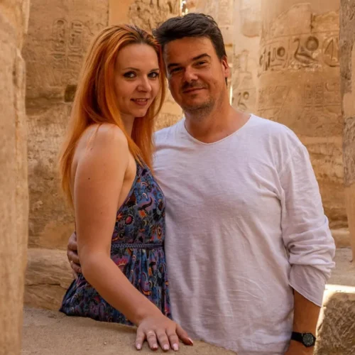 traveler couple smiling together beside an ancient pharaonic statue inside karnak temple complex in luxor