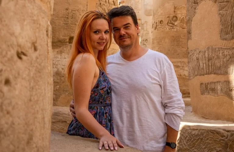 traveler couple smiling together beside an ancient pharaonic statue inside karnak temple complex in luxor