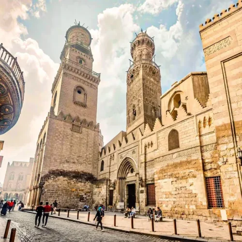 Cobblestone Al-Muizz Street lined with ornate Mamluk minarets and stone facades