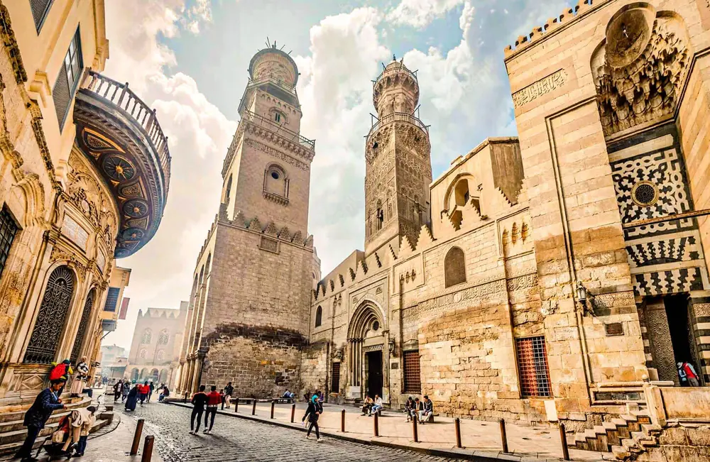 Cobblestone Al-Muizz Street lined with ornate Mamluk minarets and stone facades