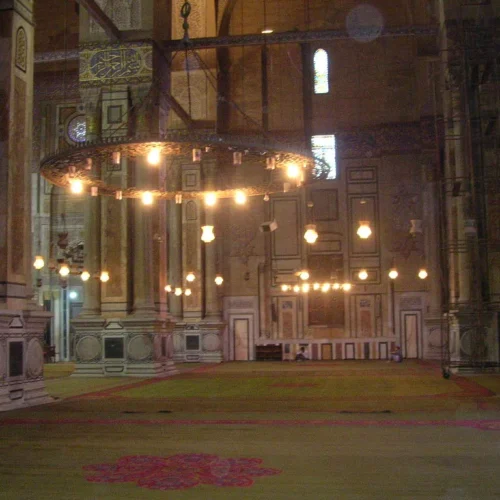 Prayer hall of Al-Rifa'i Mosque with stone pillars and a circular chandelier