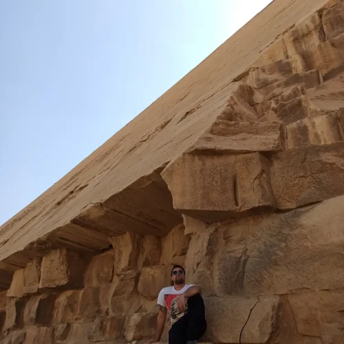 Man leaning against the massive limestone blocks of the Red Pyramid at Dahshur