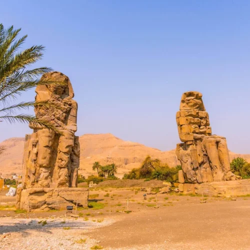 happy traveler couple posing in front of the giant quartzite colossi of memnon statues on luxor west bank