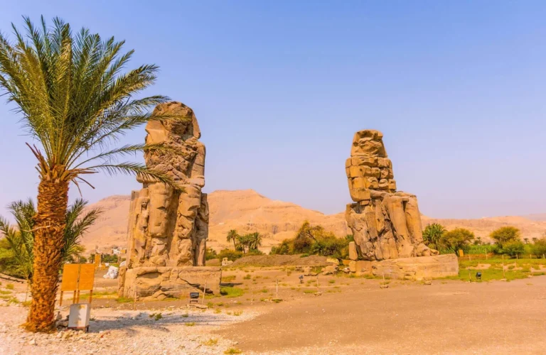 happy traveler couple posing in front of the giant quartzite colossi of memnon statues on luxor west bank