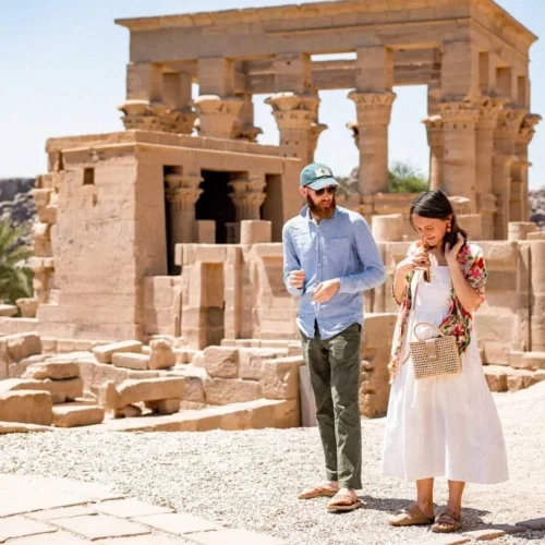 smiling traveler couple standing together in the stone colonnade courtyard of philae temple island in aswan