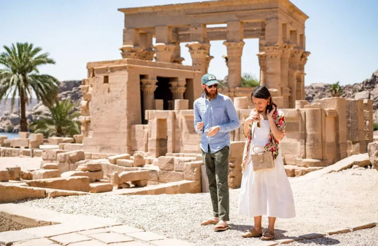 smiling traveler couple standing together in the stone colonnade courtyard of philae temple island in aswan