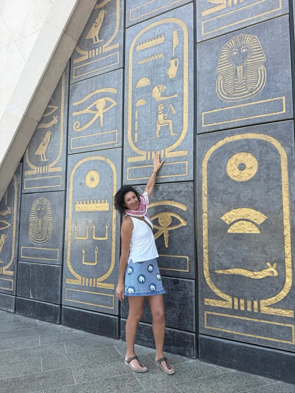 Traveler touching the gold hieroglyph and cartouche wall at the museum entrance