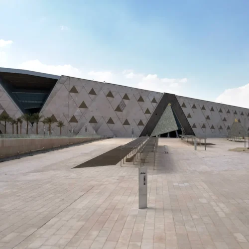 The Grand Egyptian Museum exterior with its pyramid-shaped facade, obelisk and palm-lined plaza