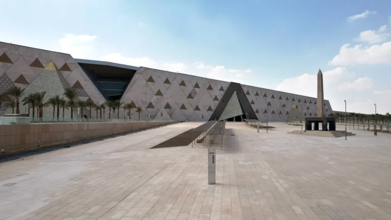 The Grand Egyptian Museum exterior with its pyramid-shaped facade, obelisk and palm-lined plaza