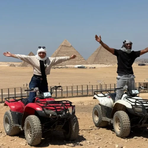 Couple standing on red and white ATVs with arms raised before the Giza pyramids