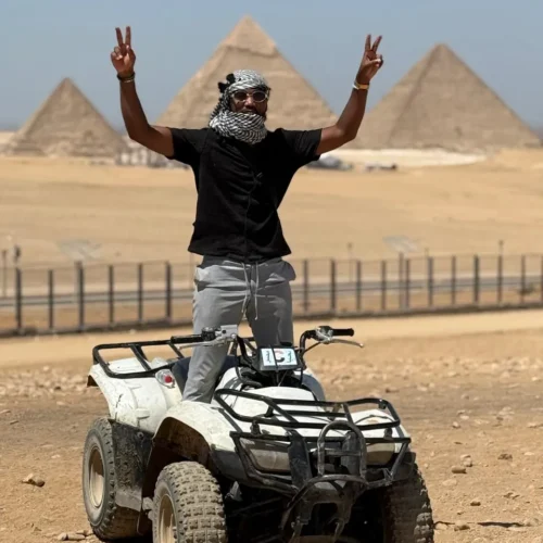 Traveler standing on a quad bike with peace signs and the Giza pyramids behind
