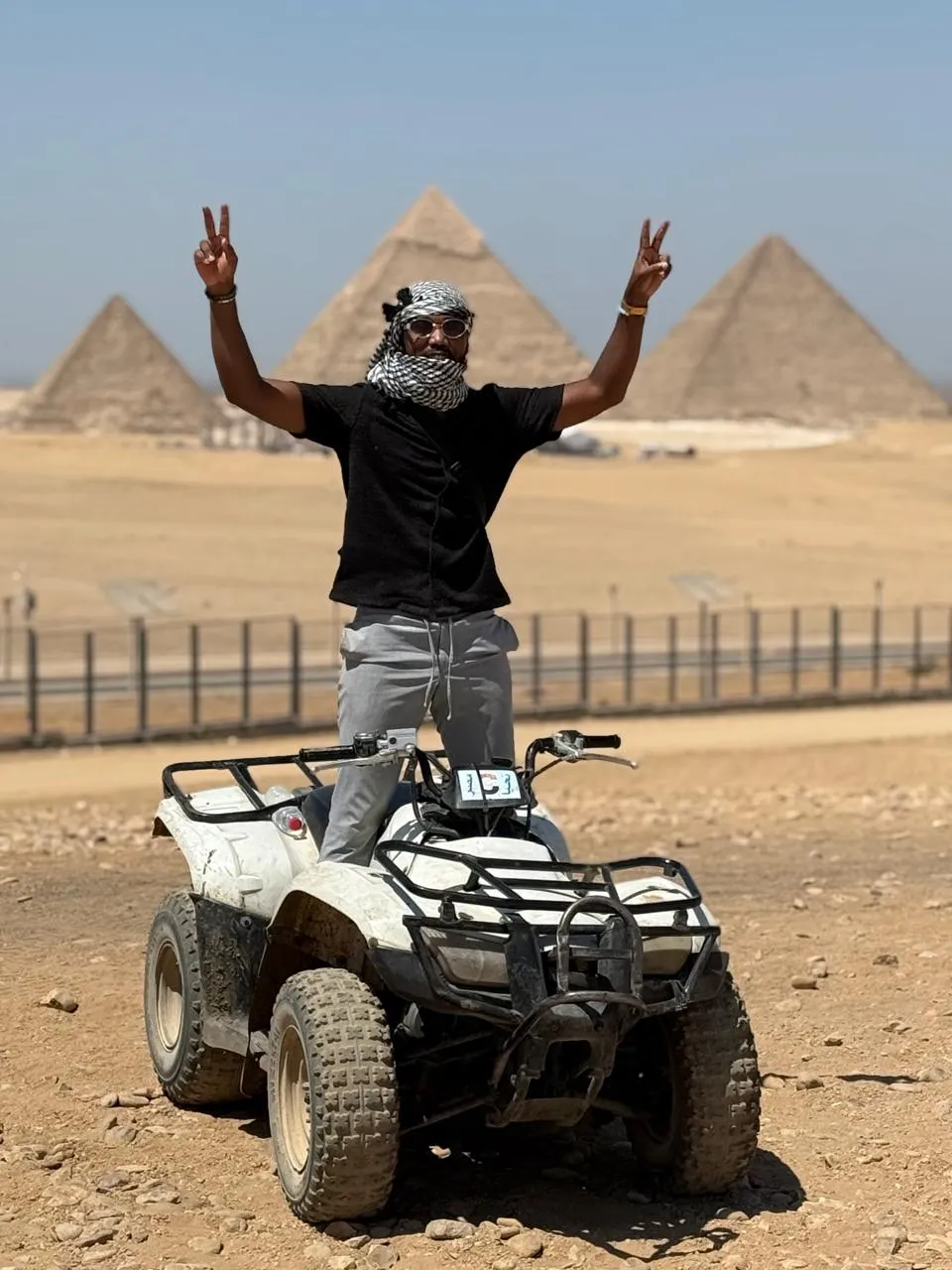 Traveler standing on a quad bike with peace signs and the Giza pyramids behind