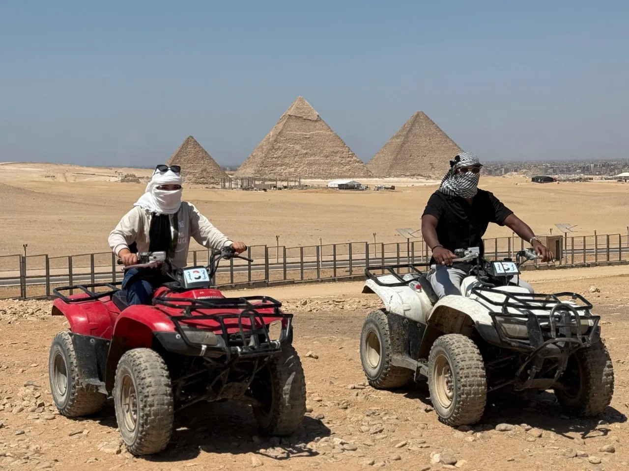 Two ATV riders facing each other with the three Giza pyramids behind