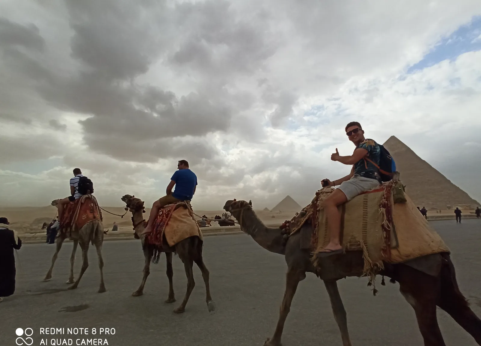 Travelers riding camels across the Giza Plateau with pyramids behind