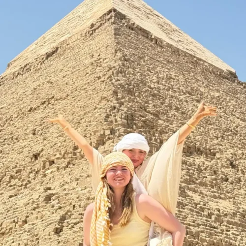 Two travelers with arms raised in front of the Pyramid of Khafre