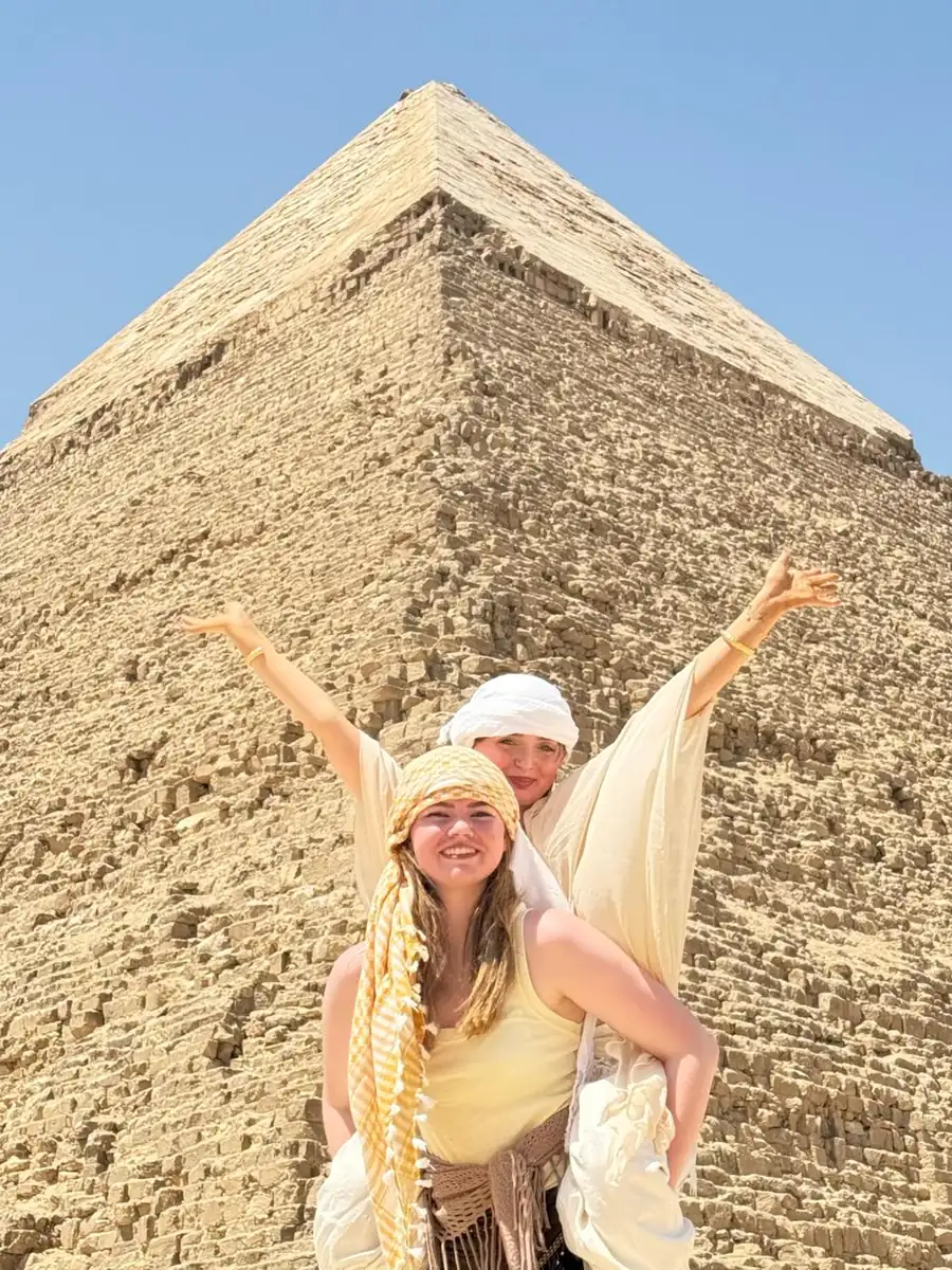 Two travelers with arms raised in front of the Pyramid of Khafre