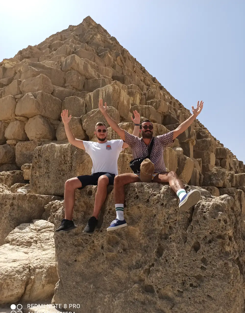 Two travelers seated with arms raised on the blocks of a Giza pyramid