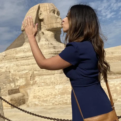 Traveler in a navy dress posing to kiss the Great Sphinx of Giza
