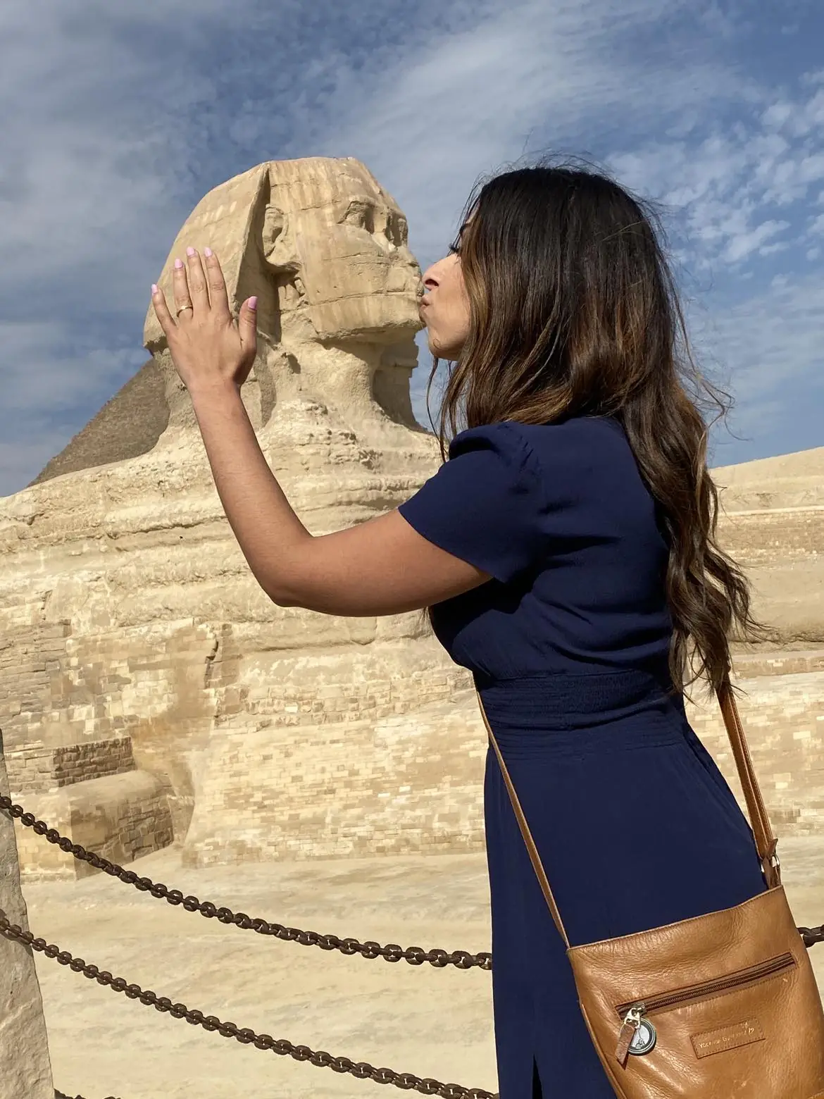 Traveler in a navy dress posing to kiss the Great Sphinx of Giza