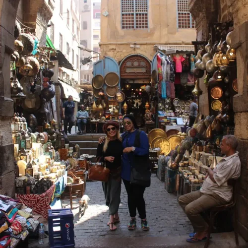 Two travelers posing in a lantern-lined alley of Khan El Khalili bazaar