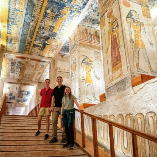 travelers walking through a vibrant painted corridor inside an ancient tomb in valley of the kings luxor