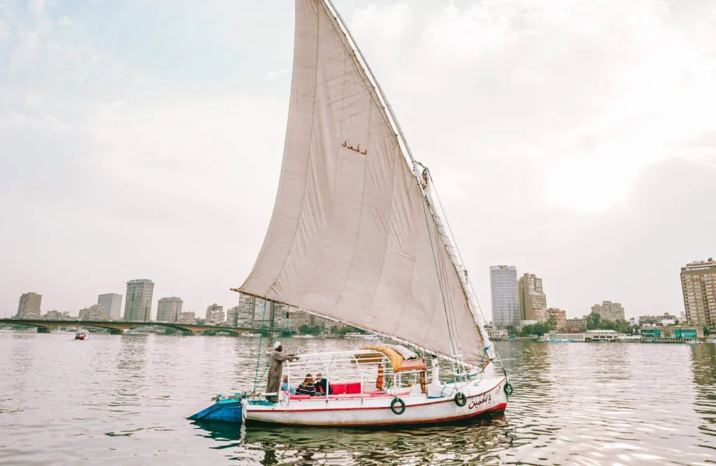 White felucca with a full lateen sail cruising the Nile past the Cairo skyline
