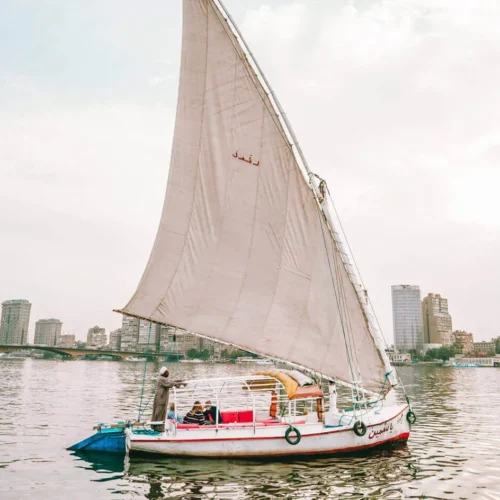 White felucca with a full lateen sail cruising the Nile past the Cairo skyline