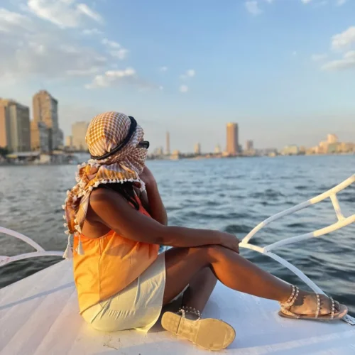 Traveler in a yellow keffiyeh sitting on the bow of a Nile boat facing Cairo