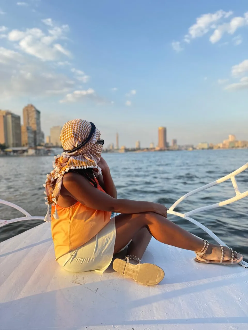 Traveler in a yellow keffiyeh sitting on the bow of a Nile boat facing Cairo