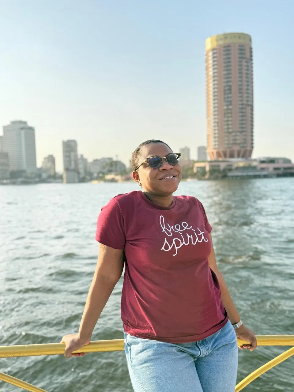 Traveler leaning on a yellow boat railing with the Nile and Cairo skyline behind