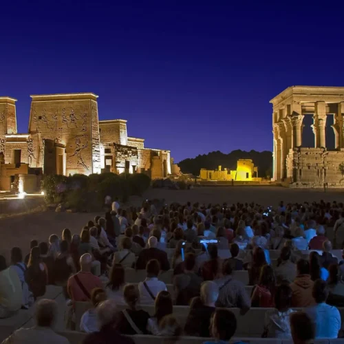 visitors watching the dramatic evening illumination of philae temple pylon during the sound and light show in aswan