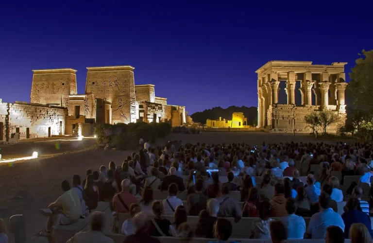 visitors watching the dramatic evening illumination of philae temple pylon during the sound and light show in aswan