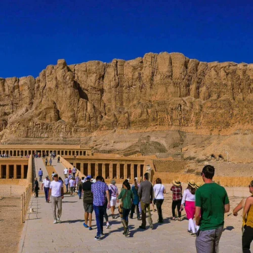 travelers walking across the limestone terrace toward temple of hatshepsut on luxor west bank