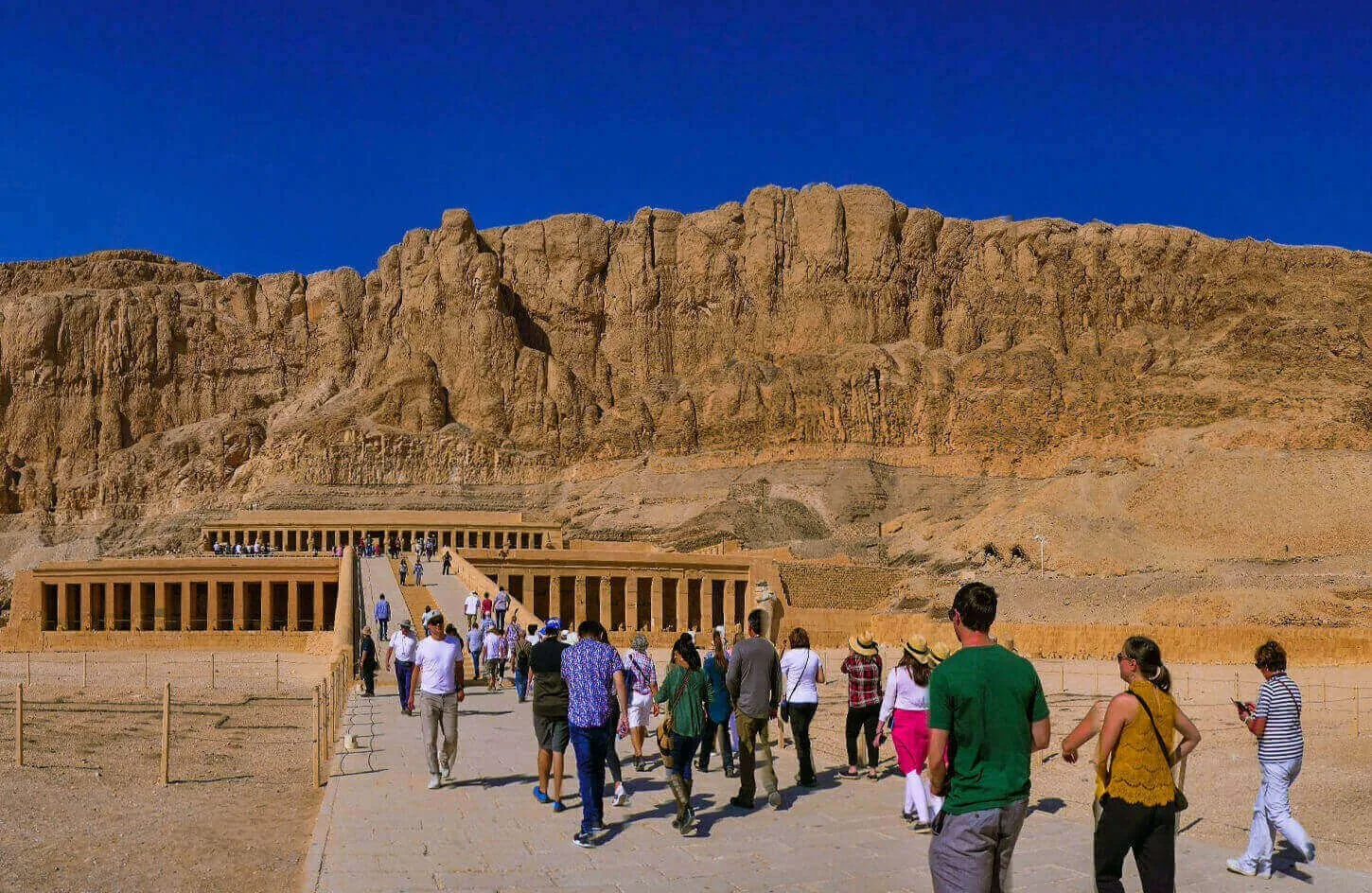 travelers walking across the limestone terrace toward temple of hatshepsut on luxor west bank