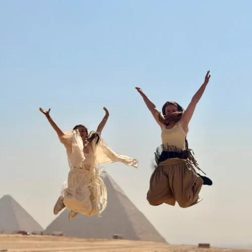 Two travelers jumping for joy in front of the Giza pyramids