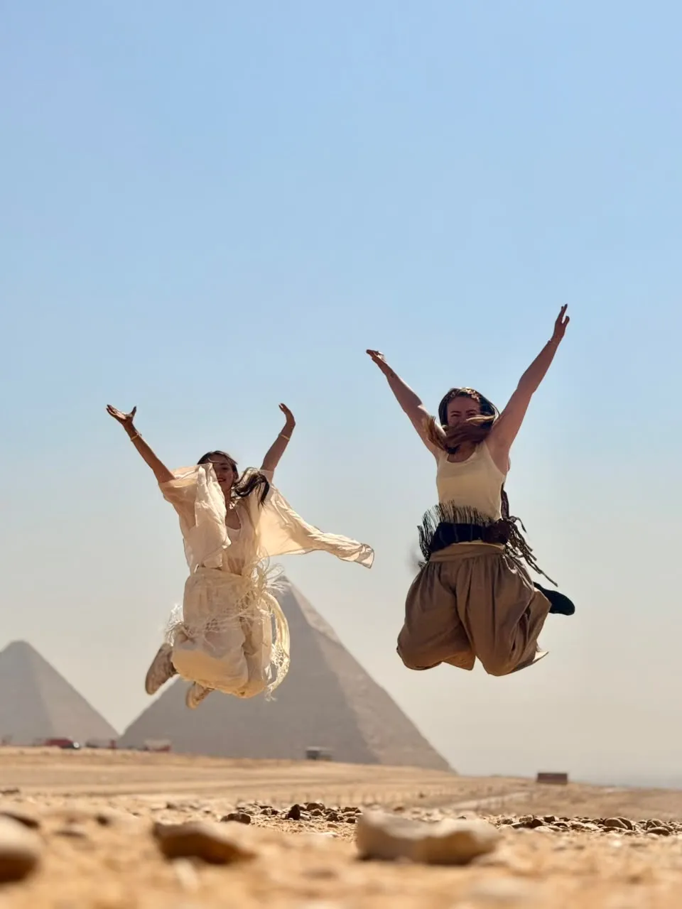 Two travelers jumping for joy in front of the Giza pyramids
