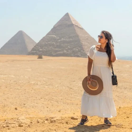 Traveler in a white dress on the Giza plateau with two pyramids behind