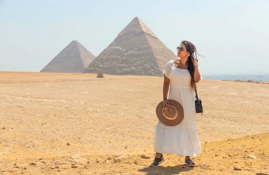 Traveler in a white dress on the Giza plateau with two pyramids behind