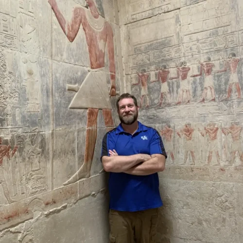 Man beside a painted relief of an ancient Egyptian figure inside a Saqqara noble's tomb