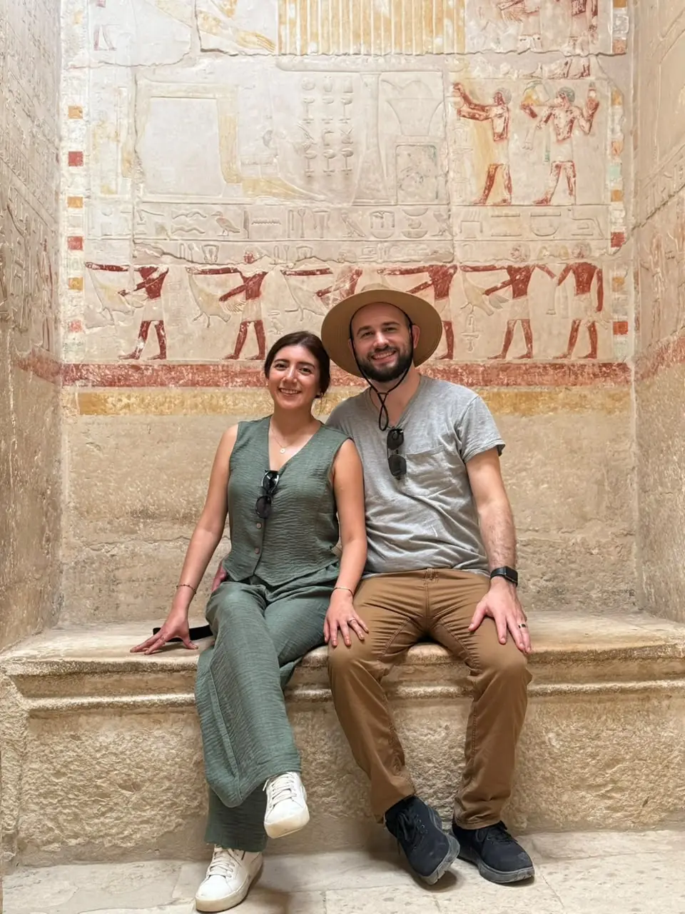 Couple seated below colourful painted reliefs inside a Saqqara noble's tomb