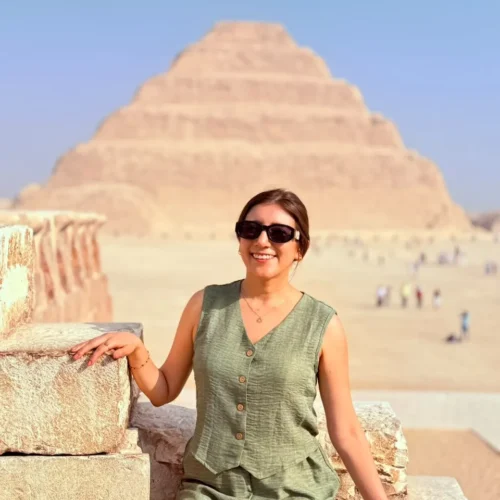 Woman seated on a stone wall with the Step Pyramid of Djoser rising behind her at Saqqara