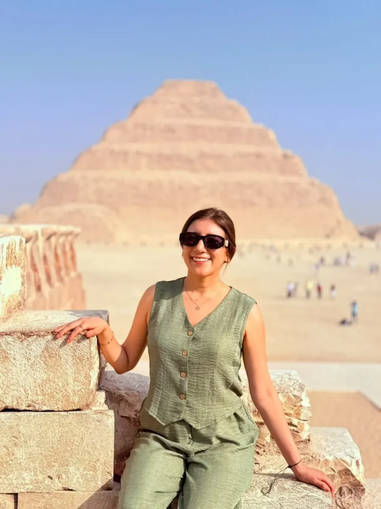 Woman seated on a stone wall with the Step Pyramid of Djoser rising behind her at Saqqara