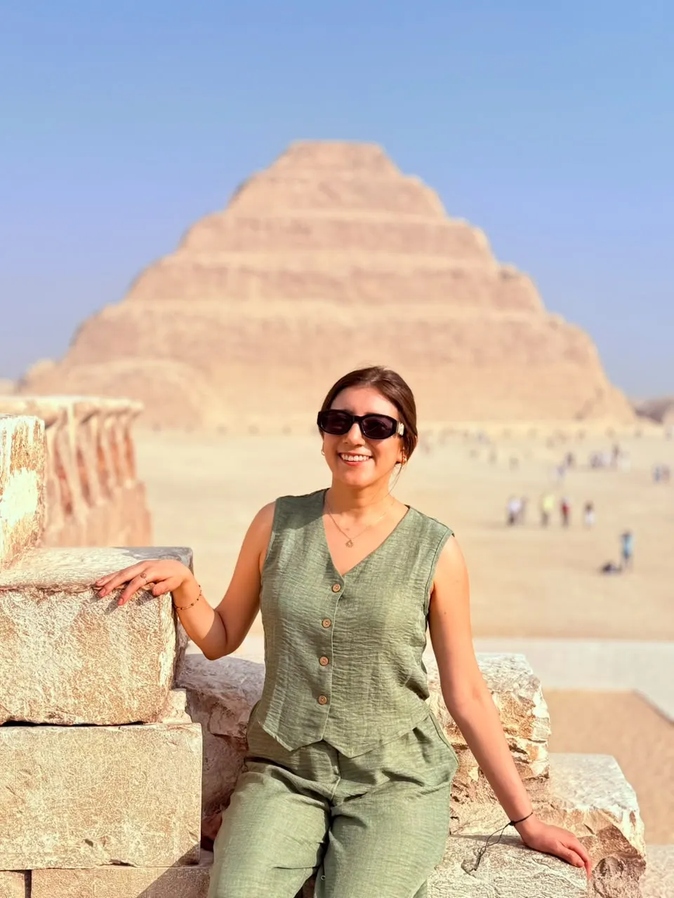 Woman seated on a stone wall with the Step Pyramid of Djoser rising behind her at Saqqara