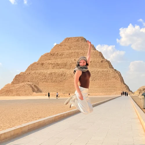 Traveler jumping with joy on the paved walkway in front of the Step Pyramid of Djoser at Saqqara
