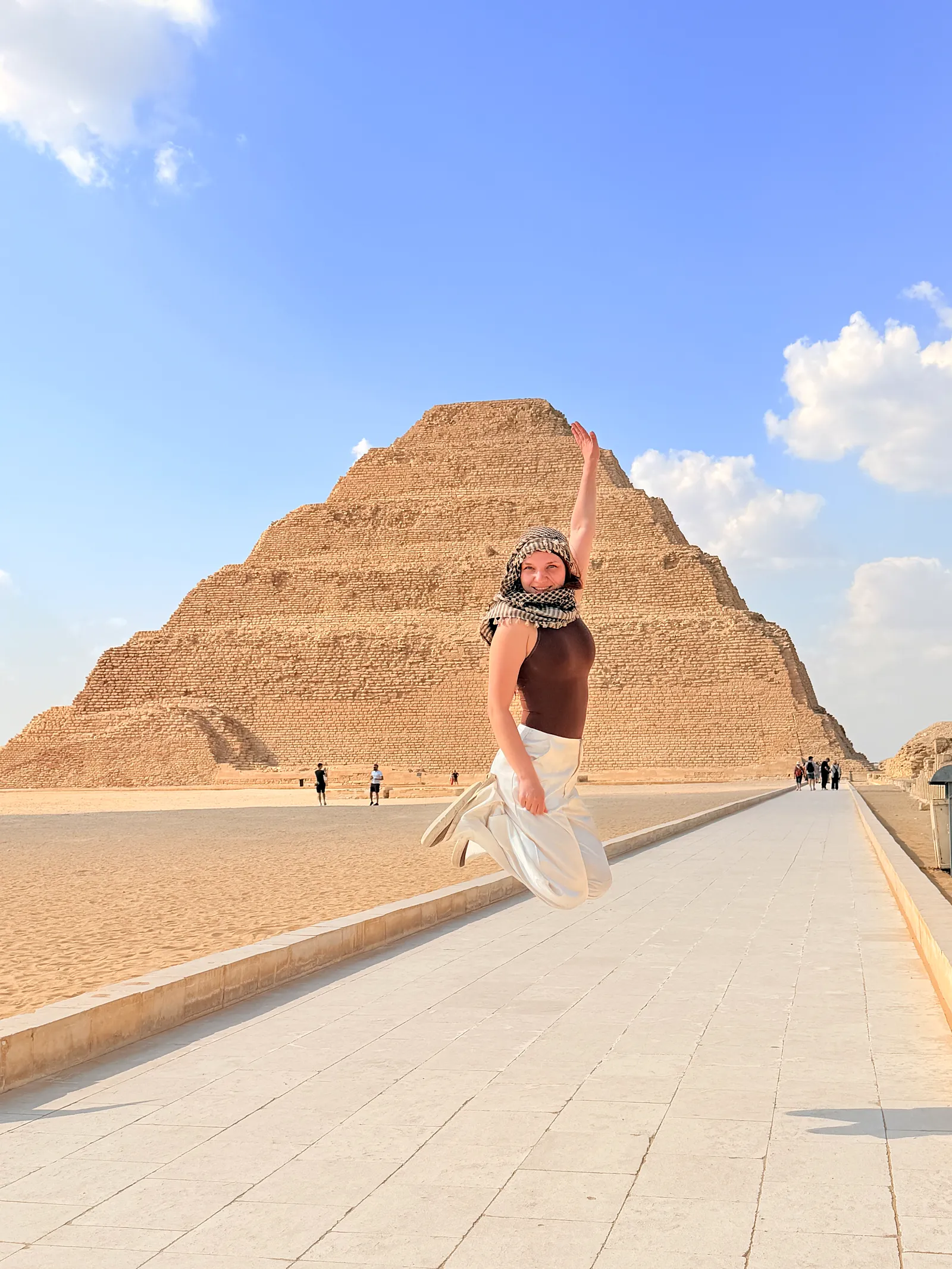 Traveler jumping with joy on the paved walkway in front of the Step Pyramid of Djoser at Saqqara