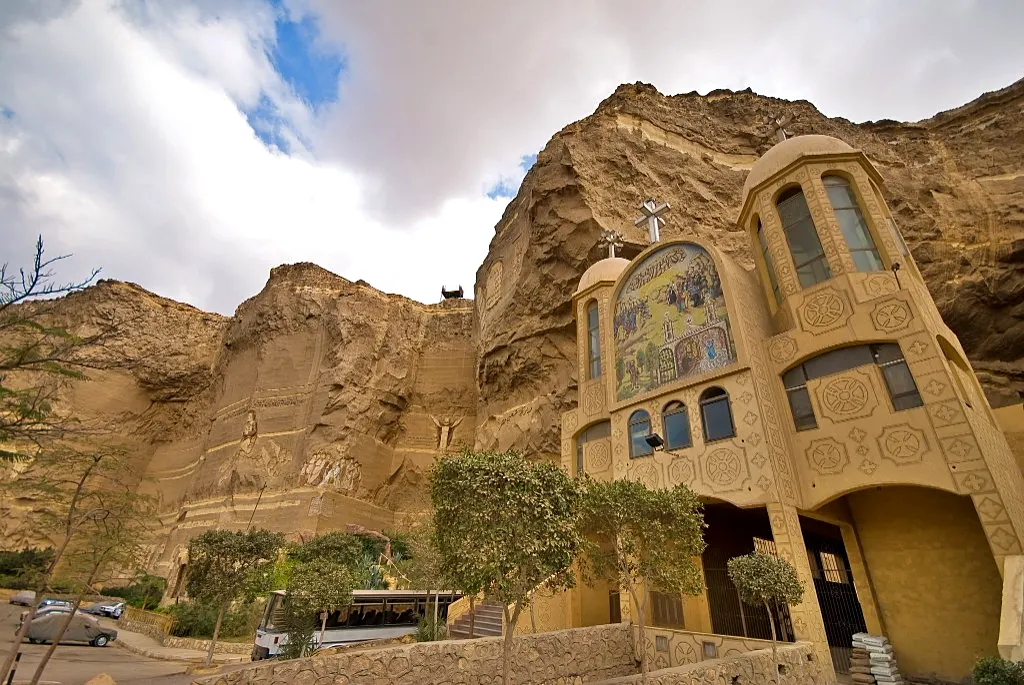 Monastery of St. Simon the Tanner built into the Mokattam cliff in Cairo, with Coptic domes, a facade mosaic, and rock carvings