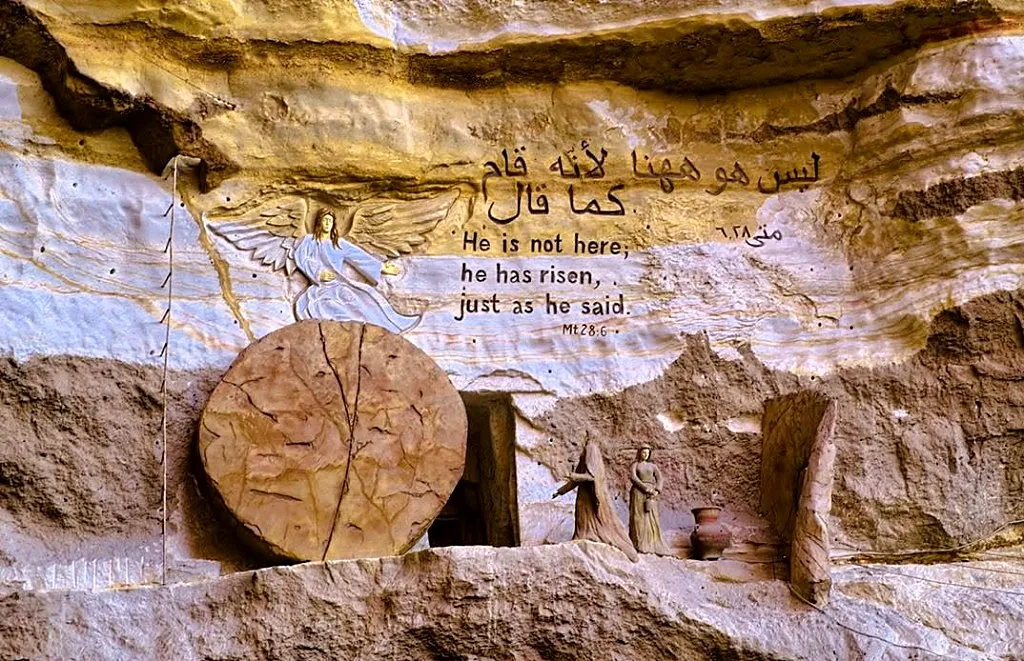 Cliff-carved Resurrection scene at St. Simon monastery with empty tomb, rolled stone, angel relief, and Matthew 28:6 text